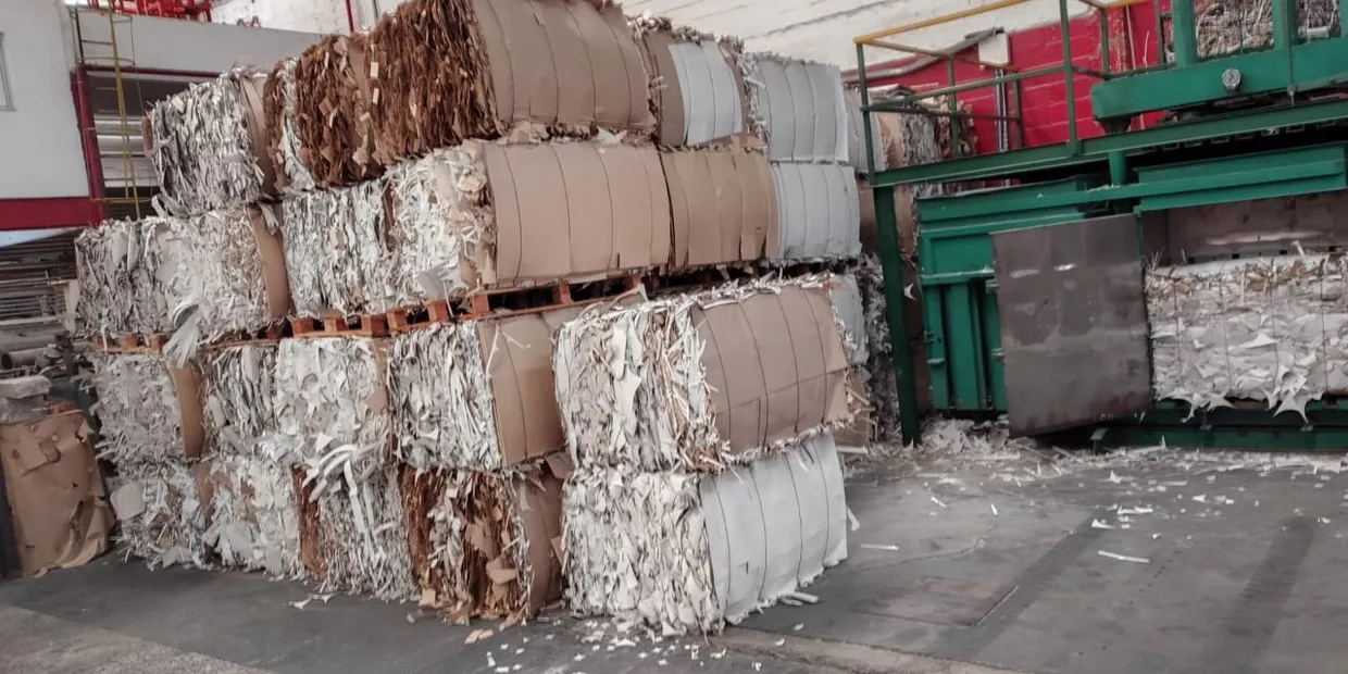 Fardos de papel recuperado apilados junto a la línea, listos para volver al proceso